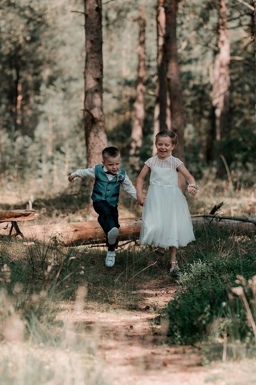 Bruidsjonker en bruidsmeisje springen lachend over een boomstam in het bos