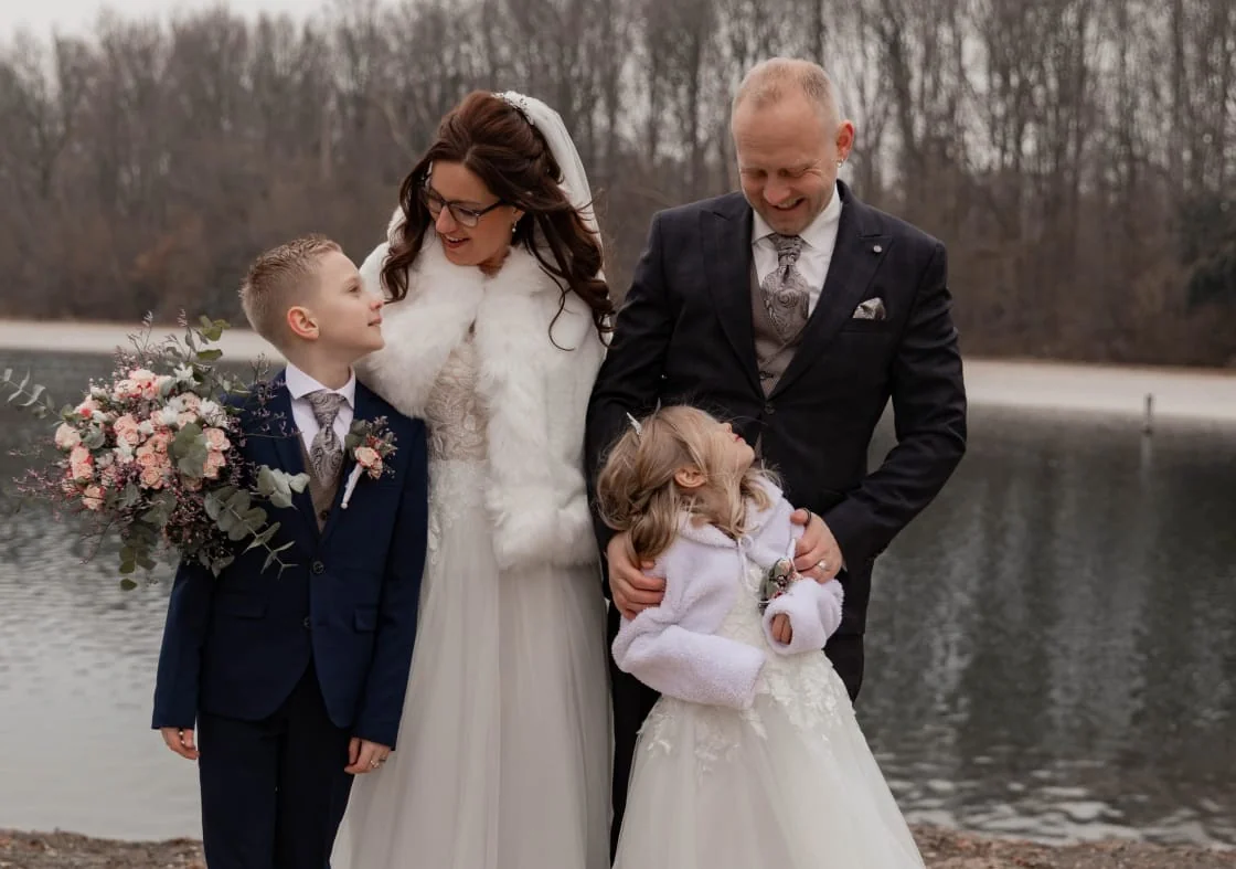Bruidspaar met zoon en dochter aan het water in de winter, de bruid met een witte stola