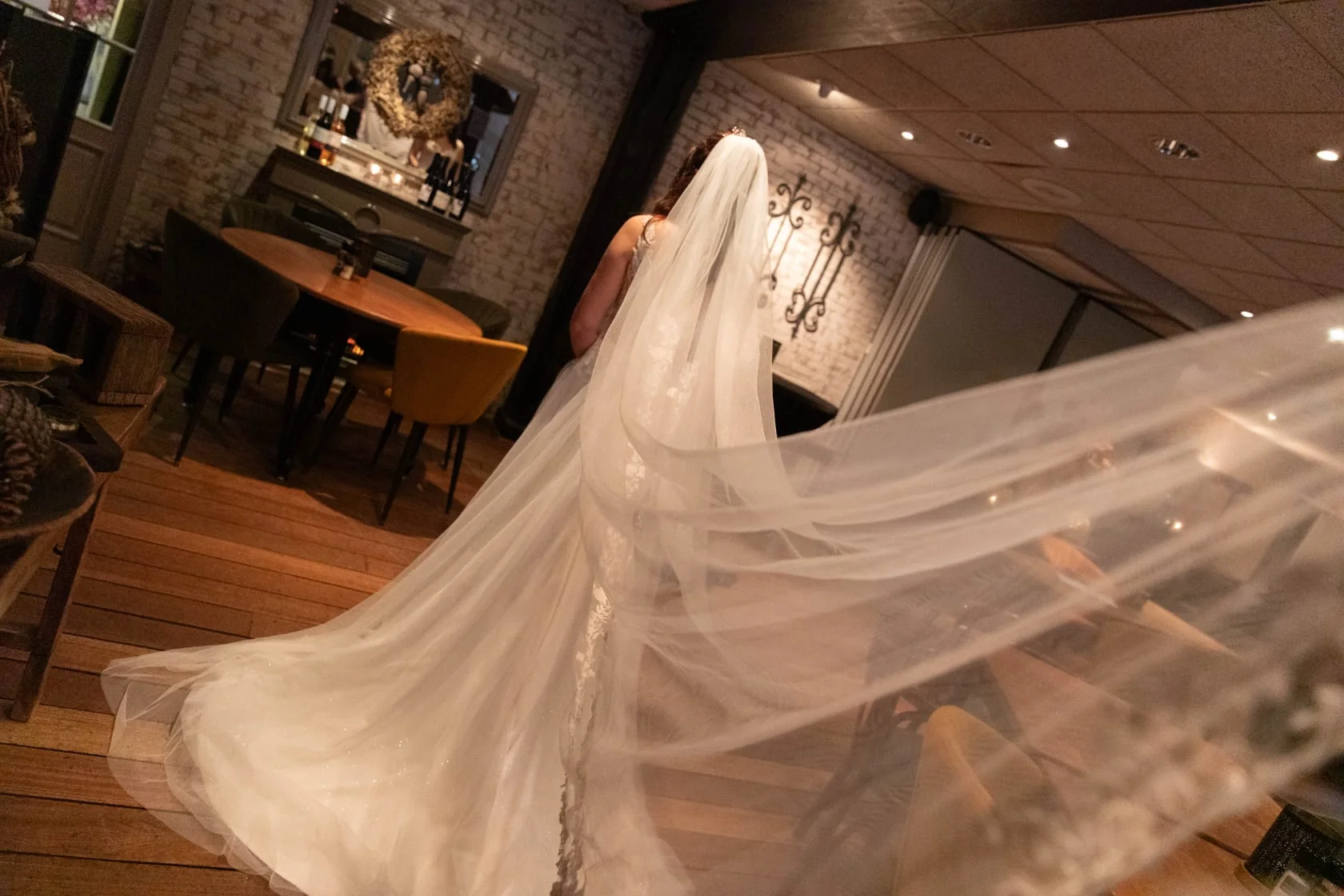 Bruid in een sfeervolle zaal, haar lange sluier waait door de ruimte
