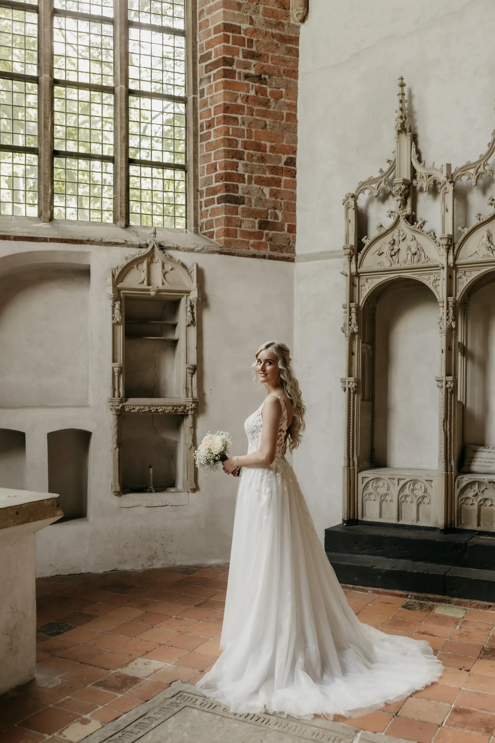 Bruid in een oude kerk in een tule jurk met een lange sleep