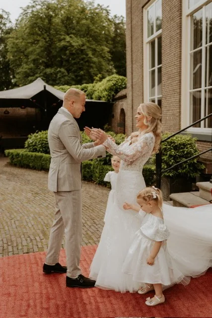 Bruidspaar op een rode loper voor een landhuis, met twee kleine bruidsmeisjes