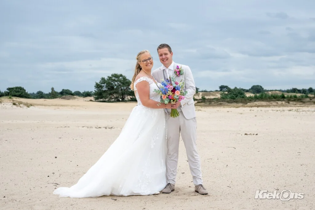Lachend bruidspaar op het zand met een kleurrijk boeket