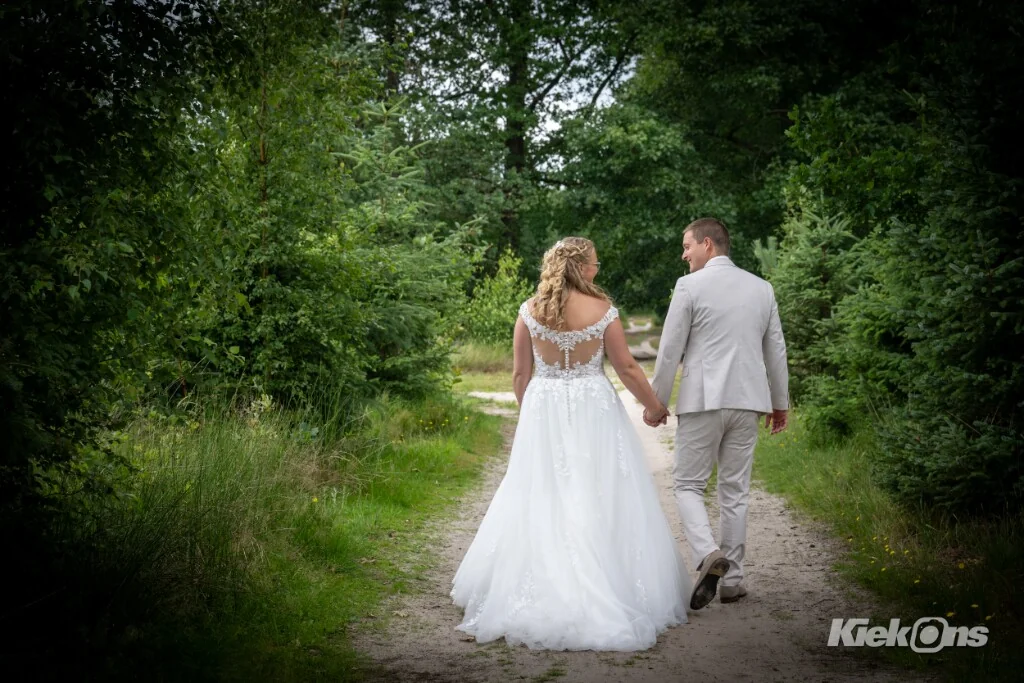 Bruidspaar loopt hand in hand over een bospad