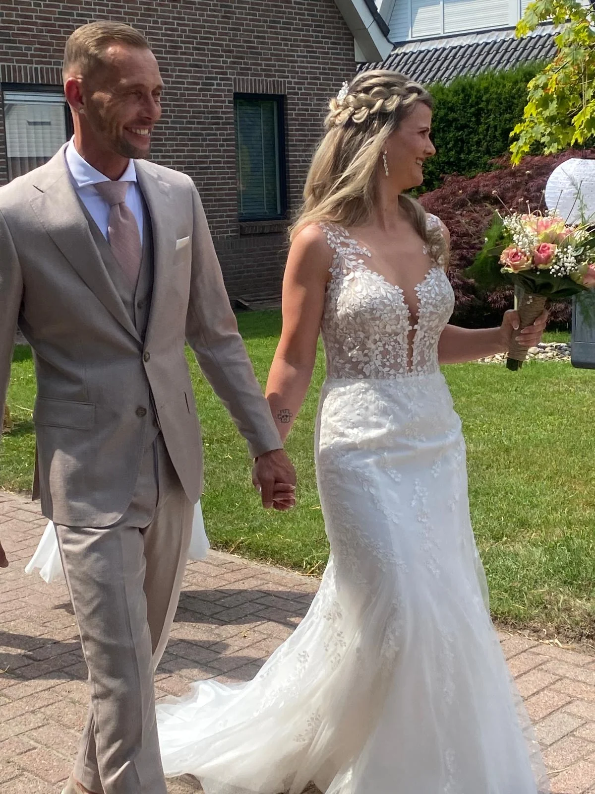 Bruidspaar loopt lachend hand in hand, de bruid met een boeket roze rozen