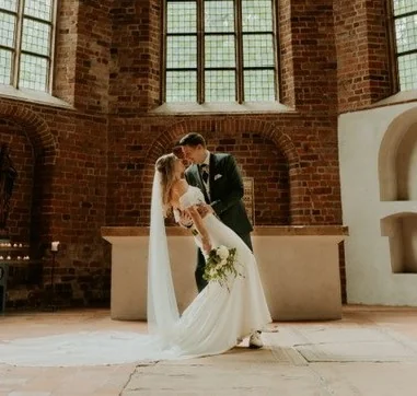 Bruidegom buigt zijn bruid achterover voor een kus in een kerk