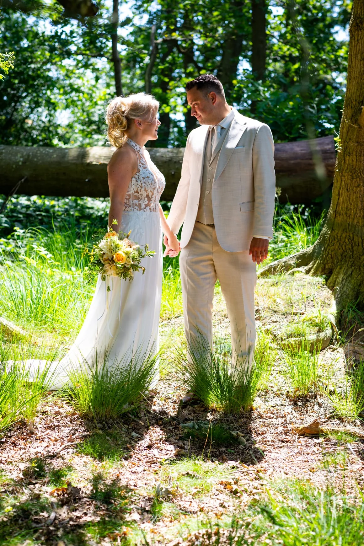 Bruidspaar hand in hand in een zonnig bos, de bruid met een geel boeket