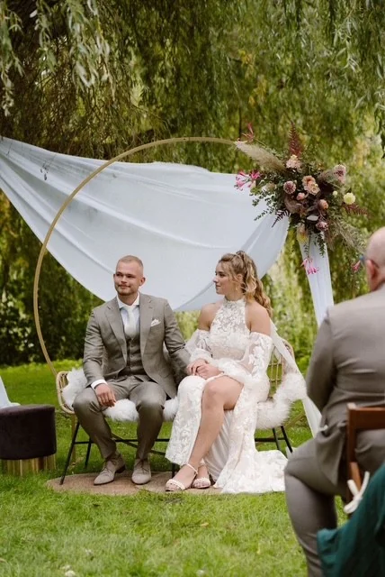 Bruidspaar zit tijdens de ceremonie onder de treurwilg, voor een gouden boog