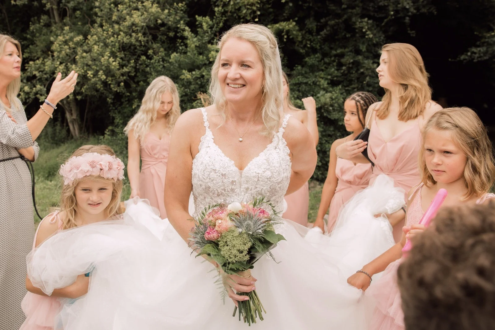 Stralende bruid met haar boeket, omringd door bruidsmeisjes in roze jurken die de rok dragen