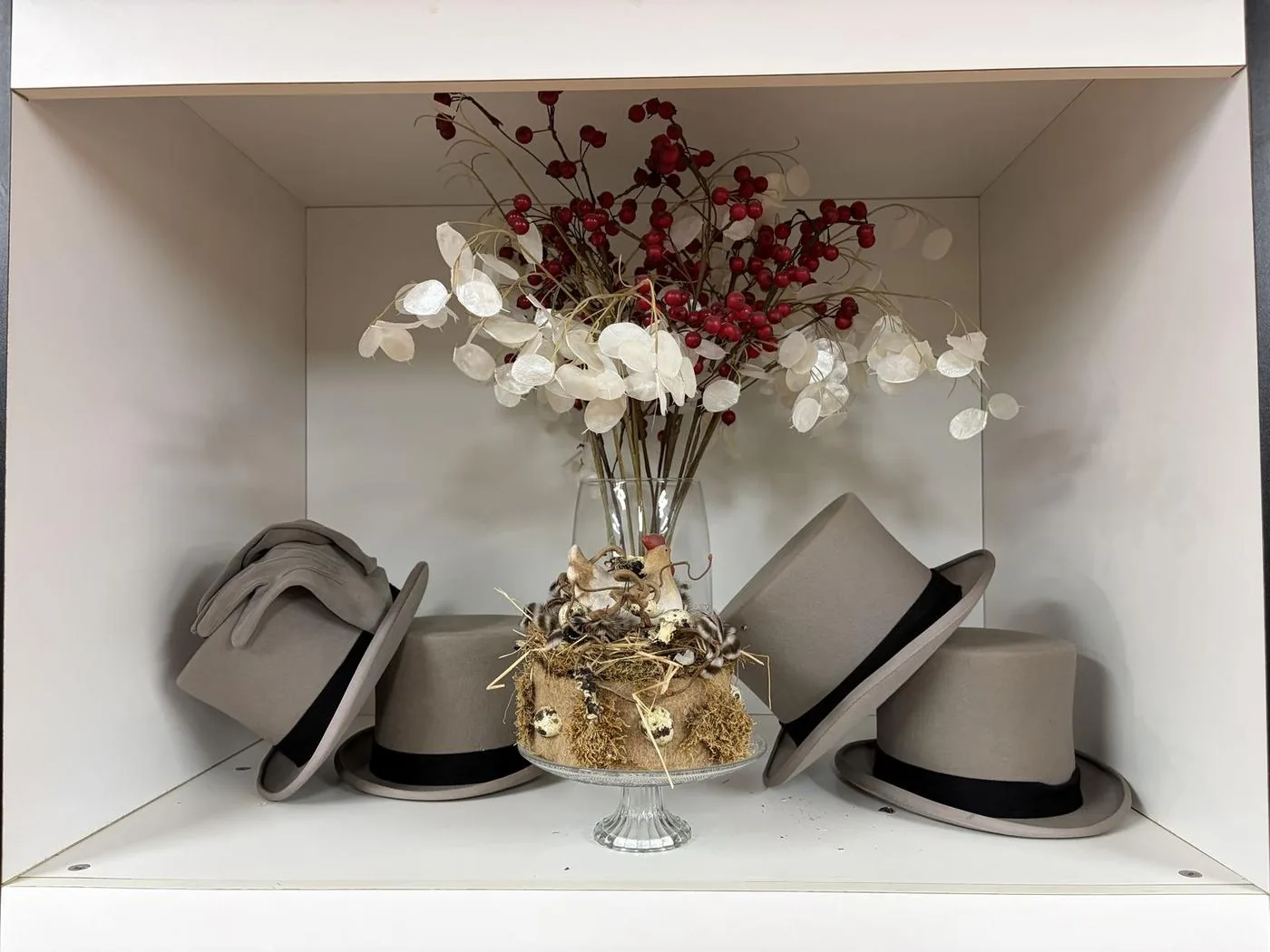 Grijze hoge hoeden in een vitrine met droogbloemen